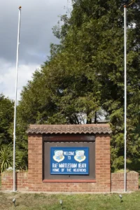 Welcome to Martlesham Heath Sign hanging at the entrance gate to the site with flag poles.